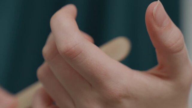 Closeup hands holding wooden stick during cuticle push, professional salon backdrop, steady grip and precise thumb motion, soft teal curtain, hygienic technique and soothing grooming ritual, focused