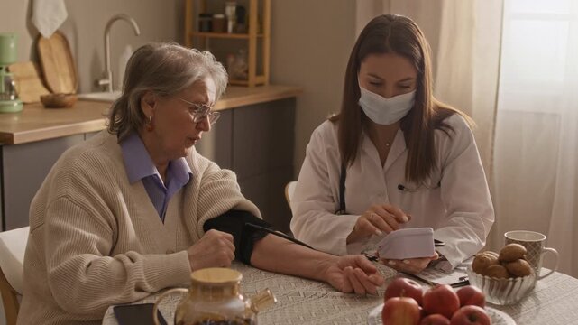 Medium shot of doctor measuring blood pressure of senior woman and having conversation about further treatment
