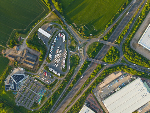 Aerial view of Rugby Services motorway service area with a large truck parking area, car parks and a highway junction surrounded by green fields in Rugby, England, United Kingdom.