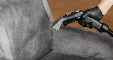 Obraz premium Professional upholstery cleaning with extraction vacuum cleaner spraying water on gray armchair
