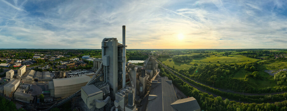 Aerial view of Rugby Cement Plant featuring industrial towers and a tall chimney overlooking green fields and the town at sunset Rugby, England, United Kingdom.