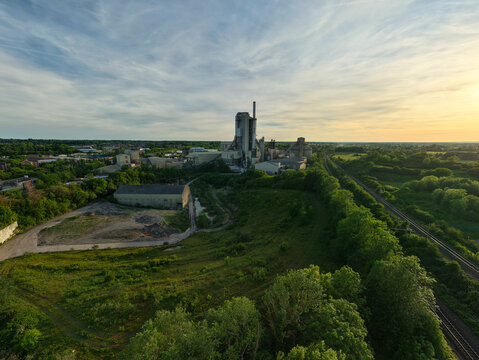 Aerial view of the Rugby Cement Plant industrial facility surrounded by lush green fields and railway tracks under a golden sunset sky Rugby, England, United Kingdom.