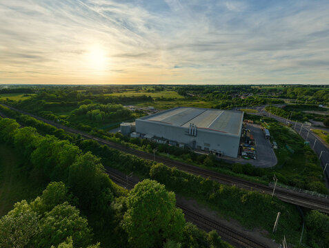 Aerial view of the Rugby Cement Plant and industrial warehouse next to railway tracks and green fields under a golden sunset in Rugby, England, United Kingdom.