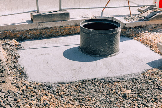 Concrete foundation supporting a newly installed sewer shaft, surrounded by gravel and soil at a road construction site