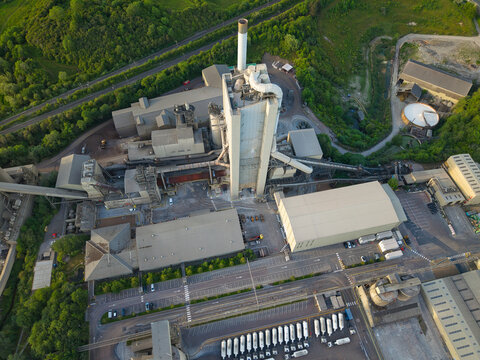 Aerial view of the Rugby Cement Plant featuring its tall industrial tower, sprawling factory buildings, and lush green hills in Rugby, England, United Kingdom.