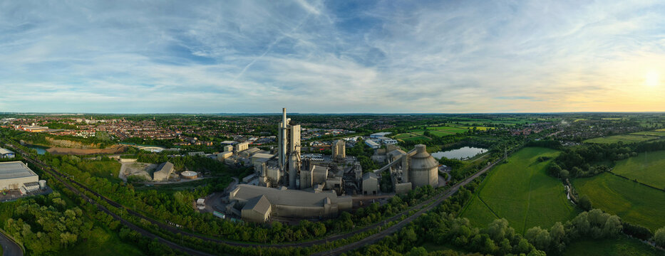 Aerial view of the Rugby Cement Plant with its tall chimneys and industrial silos surrounded by green fields and the town skyline Rugby, England, United Kingdom.