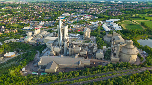 Aerial view of the Rugby Cement Plant featuring tall chimneys and industrial structures surrounded by lush greenery in Rugby, England, United Kingdom.