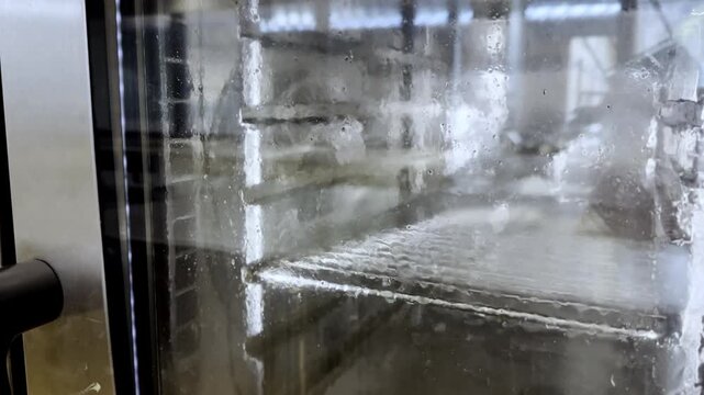 Detailed view of a professional food service baking oven undergoing a self-wash maintenance cycle, with clean water heavily cascading down the interior of the glass door to maintain strict restaurant 