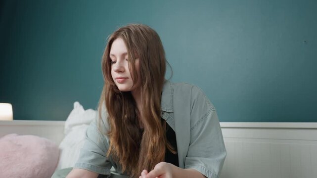 Caucasian teen sipping drink while tending nails bedside, relaxed crosslegged pose, amber beverage in glass, contemplative expression, soft bedside lamp, mellow evening ritual and home comfort