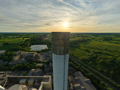 Aerial view of the Rugby Cement Plant chimney overlooking industrial facilities and green countryside during sunset Rugby, England, United Kingdom.