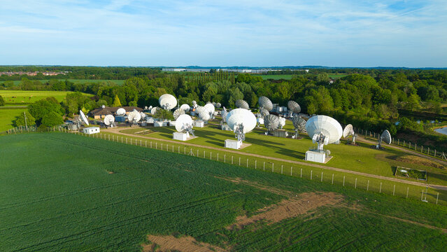 Aerial view of the Satellite Mediaport ground station with large parabolic dishes on a grassy field surrounded by green trees and farmland in Long Lawford, England, United Kingdom.