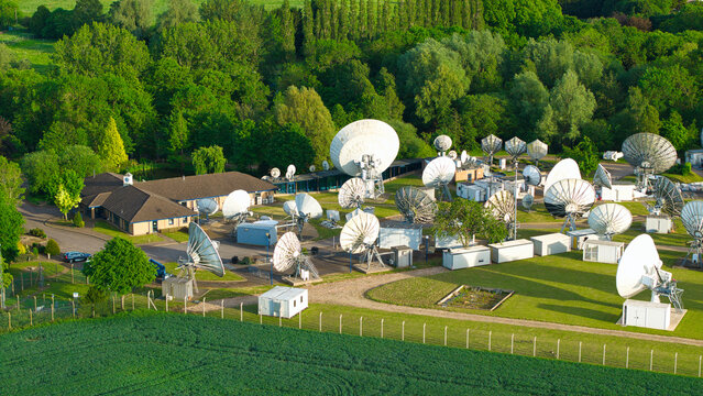 Aerial view of the Satellite Mediaport featuring numerous parabolic antennas surrounded by lush green trees and fields in Long Lawford, England, United Kingdom.