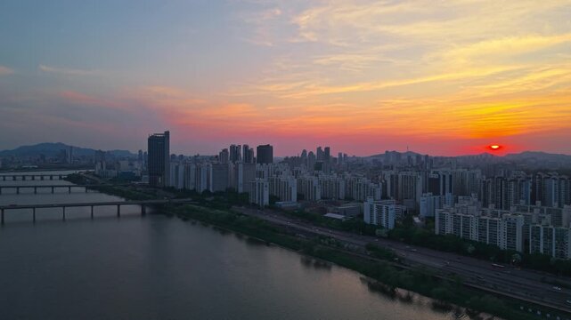 Aerial pullback along Gangbyeonbuk-ro Expressway traffic and Gwangjin District in Seoul with colorful sunset sky over Han River South Korea