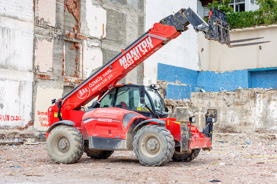 8 May 2026, Kusadasi, Turkiye: Red Manitou telehandler with raised forks demolishing a brick and concrete urban building at a dusty construction site