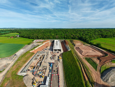Aerial view of HS2 High Speed Rail Civil Engineering Works with a concrete tunnel portal, construction machinery, and excavated earth near green fields in Southam, England, United Kingdom.