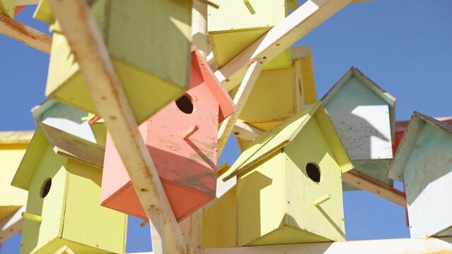 Colorful wooden birdhouses are arranged together, forming an abstract and vibrant community structure offering shelter and protection under a clear blue sky, symbolizing unity and togetherness