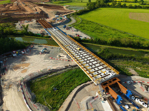 Aerial view of HS2 High Speed Rail Civil Engineering Works bridge construction over a canal with machinery and green fields in Southam, England, United Kingdom.