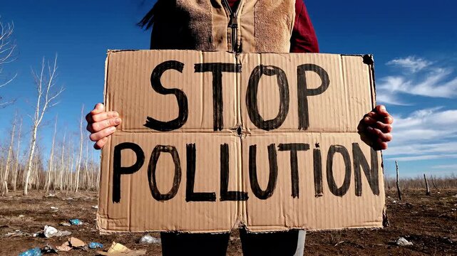 Person holding stop pollution cardboard sign.