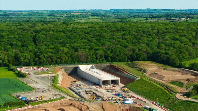 Aerial view of HS2 High Speed Rail Civil Engineering Works featuring a concrete tunnel portal, construction machinery, and dense woodland Southam, England, United Kingdom.