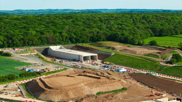 Aerial view of HS2 High Speed Rail Civil Engineering Works showing the concrete tunnel portal, earthworks, and construction machinery surrounded by lush woodland Southam, England, United Kingdom.
