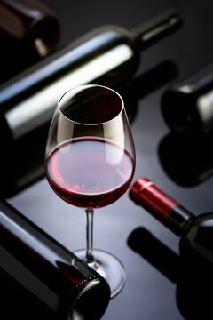 Glass and bottles of red wine on a black reflective background.