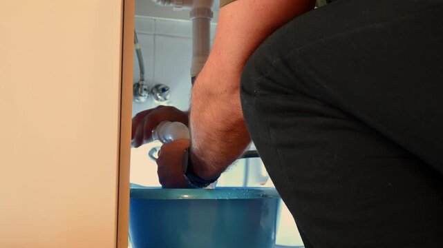 Plumber cleaning clogged sink siphon under the basin