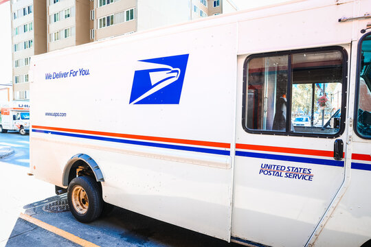 Close-up profile of a classic USPS mail van with the blue eagle logo and United States Postal Service text on the driver side door.