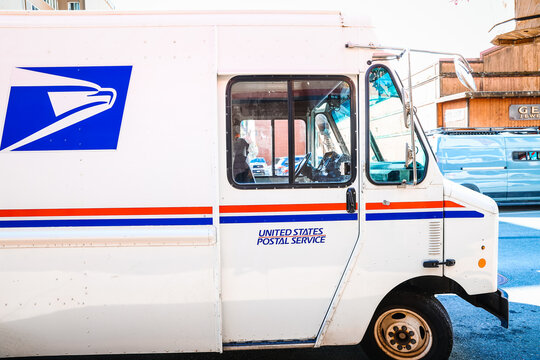 Close-up profile of a classic USPS mail van with the blue eagle logo and United States Postal Service text on the driver side door.
