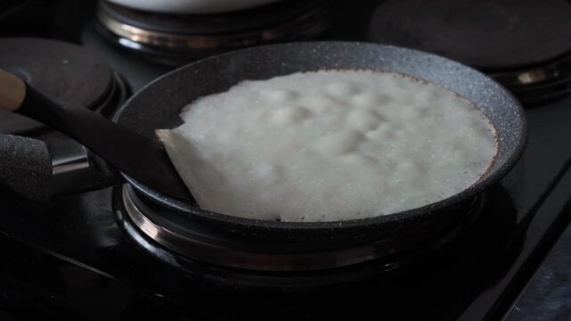 The process of baking a pancake in a pan, where the edge of the finished golden pancake is lifted with a spatula