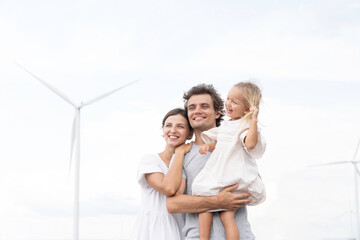 Fototapeta premium Happy caucasian family, father, mother and little daughter travel at wind turbine field farm on holiday weekend