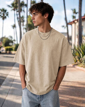 Beige t-shirt mockup on male model standing outdoor with palm trees background. Blank oversized cream tee presentation. Mens casual streetwear apparel fashion style.