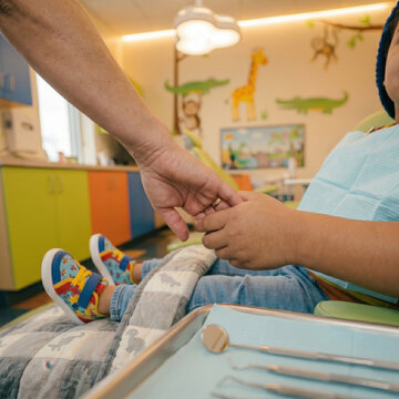 Pediatric dentist holding young child's hand in colorful dental clinic office. Reassurance, children healthcare, first visit and comforting patient procedure concept layout