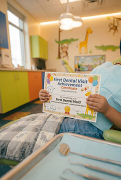 Young child holding first dental visit achievement certificate in colorful pediatric dental clinic office. Kids healthcare, reward, bravery and pediatric dentistry patient experience concept layout