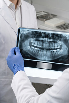 Dentist in blue medical gloves holding panoramic teeth x-ray film showing shot to colleague professional clinic diagnostic concept