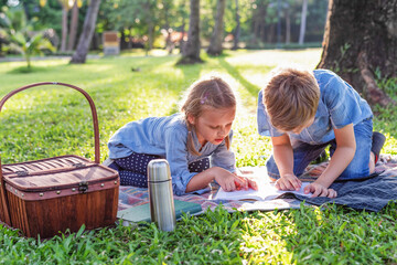 Obraz premium Two children reading on a picnic blanket in a sunny park setting.