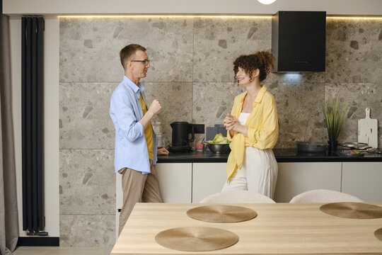 A man and woman talking in a stylish kitchen. They smile at each other, sharing ideas amidst fresh ingredients on the counter, creating a warm atmosphere of collaboration