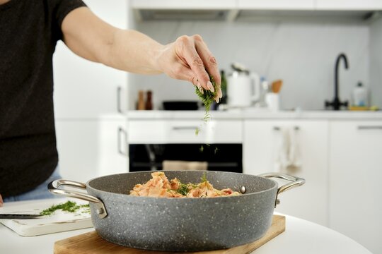 A home cook adds fresh herbs to a colorful dish in a modern kitchen. The counter showcases savory ingredients, and natural light brightens the space, creating a warm atmosphere for cooking