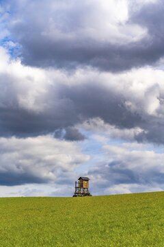 Mobile raised hide in an empty field under dramatic clouds, Brodowin ecovillage, Barnim, Brandenburg, Germany