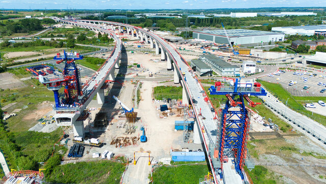 Aerial view of the HS2 Project construction site featuring a long concrete viaduct, heavy machinery, and cranes under a clear blue sky Coleshill, England, United Kingdom.