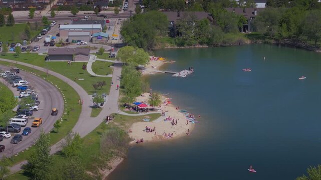Drone video of sunbathers and swimmers enjoying Quinn's Pond at Esther Simplot Park, Boise, Idaho. People relaxing on the shore and playing in the water on a sunny day.