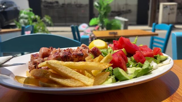 A large plate at a Greek restaurant: grilled pork souvlaki, vegetable salad, grilled potatoes, and pita bread. Greek fast food, a delicious dish &ndash; gastronomic tourism