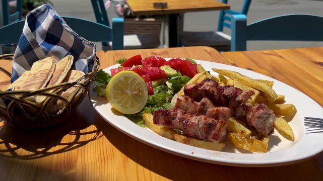 A large plate at a Greek restaurant: grilled pork souvlaki, vegetable salad, grilled potatoes, and pita bread. Greek fast food, a delicious dish &ndash; gastronomic tourism