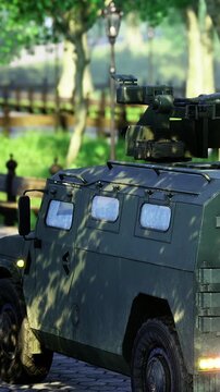 A military vehicle is parked beside a pathway in an urban setting. Green trees line the area, and street lamps stand tall. The scene shows clear daytime with no people around.