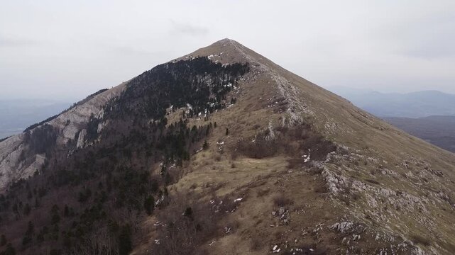Breathtaking aerial footage moving towards the famous pyramid shaped peak of Rtanj mountain in Serbia under a cloudy sky in late winter