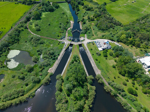 Aerial view of a canal lock system and junction surrounded by lush green fields and dense trees in Kingsbury, England, United Kingdom.