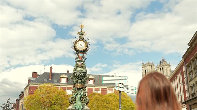 Young woman walking near historic clock tower and cathedral in Amiens France