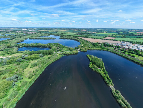 Aerial view of the interconnected lakes and lush green woodlands of Kingsbury Water Park under a clear blue sky with scattered clouds, Kingsbury, England, United Kingdom.