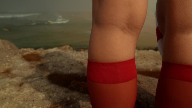 Toddler standing on beach with red socks facing ocean waves