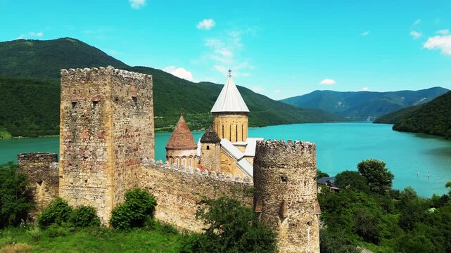 Ancient medieval castle fortress with stone walls and towers on turquoise lake shore aerial view.
