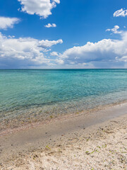 Fototapeta premium Beautiful sandy beach with crystal clear turquoise sea water under a blue sky with white clouds on a sunny day